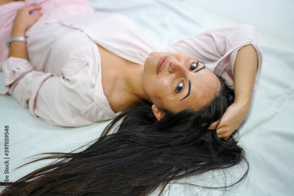 Beautiful young woman in button down shirt lying on back in bed and looking at camera Beautiful young woman in button down shirt lying on back in bed and looking at camera