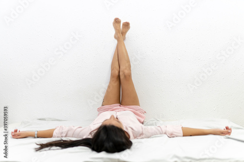 Young woman with legs up on the wall lying on bed with outstratched arms