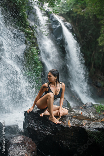 beautiful brunette sits against the background of a waterfall and washes under it.