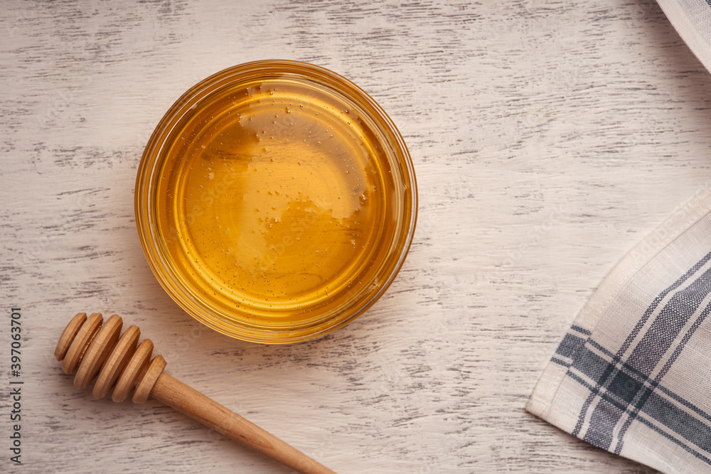 Fresh acacia honey in a glass bowl near a wooden honey spoon and towel, top view Fresh acacia honey in a glass bowl near a wooden honey spoon and towel, top view
