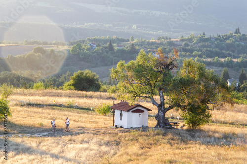 A small chapel in the middle of a meadow. In the background the hills of the mountain