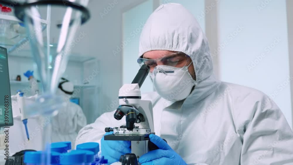 Biotechnology scientist in ppe suit researching DNA in laboratory using microscope. team examining virus evolution using high tech for scientific research of vaccine development against covid19 Biotechnology scientist in ppe suit researching DNA in laboratory using microscope. team examining virus evolution using high tech for scientific research of vaccine development against covid19