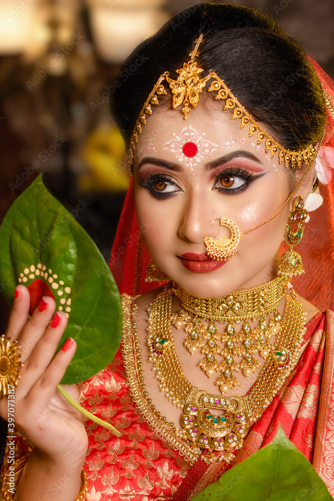 Portrait of very beautiful Indian bride holding betel leaf, Bengali bride in traditional wedding saree and makeup