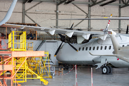 White passenger turboprop airplane under maintenance in the hangar. Repair of aircraft engine on the wing and checking mechanical systems for flight operations