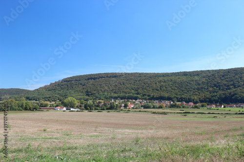 Beautiful French hilly landscape with a forest edge and a small village in the distance. Photo was taken on a summer day with blue sky.