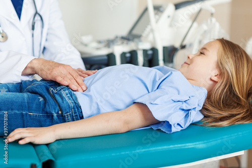 Fotografie Unrecognizable doctor palpating belly of little girl lying on couch in doctors o