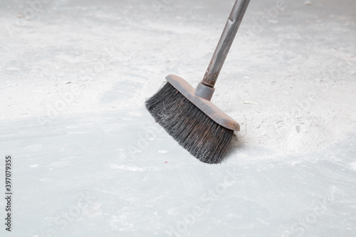 Broom sweeping white concrete dust from floor. Cleaning garbage after repair work of home. Closeup. Side view. photo
