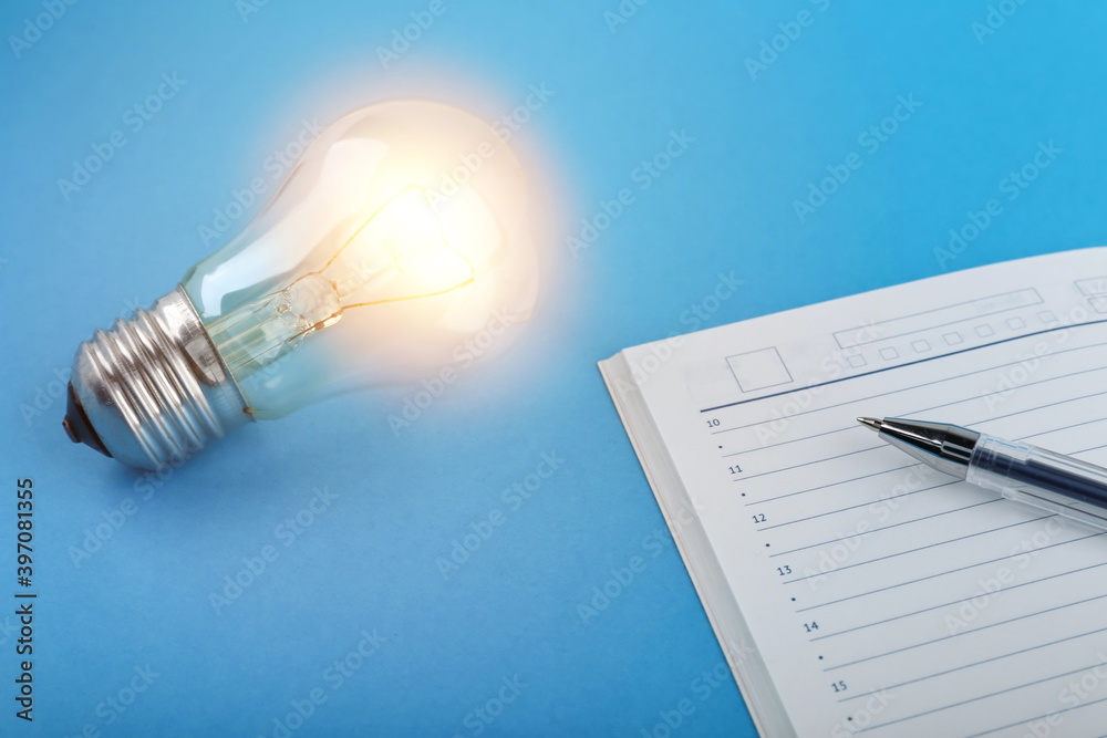 insight concept. coming of ideas at work. glowing light bulb and diary with a pen on a blue background. generation of ideas. insight concept. coming of ideas at work. glowing light bulb and diary with a pen on a blue background. generation of ideas.