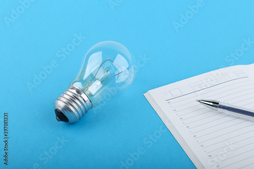 insight concept. coming of ideas at work. light bulb, diary and a pen on a blue background. generation of ideas. 