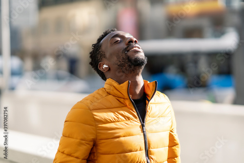 African man listening to music and breathing fresh air outdoors standing in the city photo