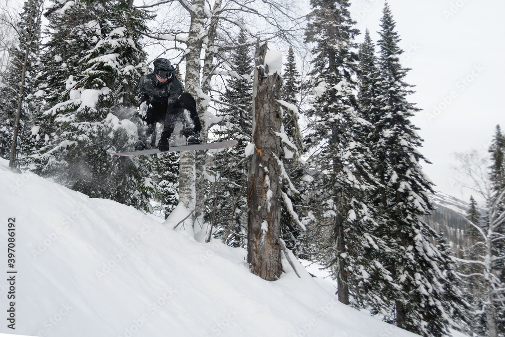 Amateur snowboarder is jumping from small kicker in the winter forest.