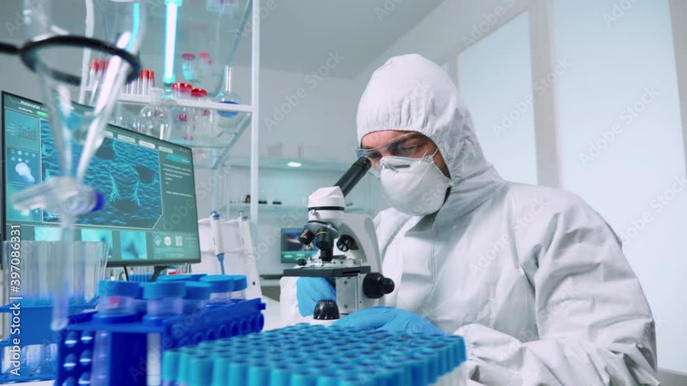Man research scientist in coverall looking at samples under microscope in modern equipped laboratory. Doctor working with various bacteria, tissue, blood tests, pharmaceutical research for antibiotics Man research scientist in coverall looking at samples under microscope in modern equipped laboratory. Doctor working with various bacteria, tissue, blood tests, pharmaceutical research for antibiotics