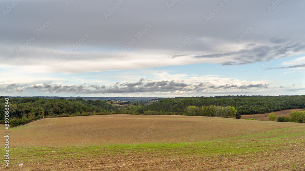 Naklejka premium Bare field at the end of winter, on the horizon the hills and the sky with cottony clouds