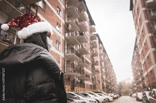 Woman stands with xmas hat in street surounded by block houses. Self histmas holidays. photo