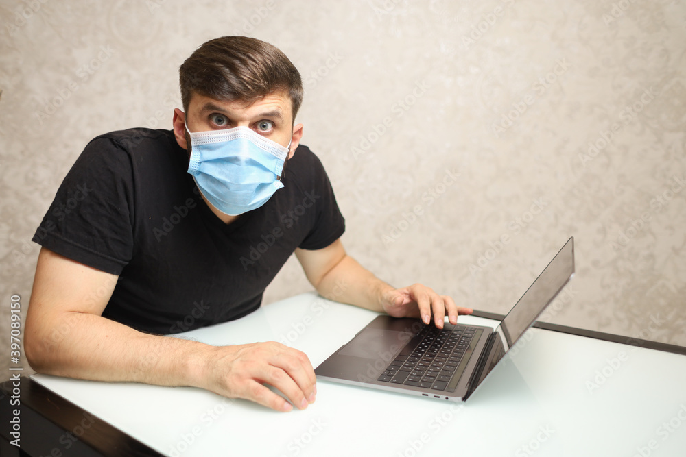 a man in a medical mask on self-isolation works at a laptop