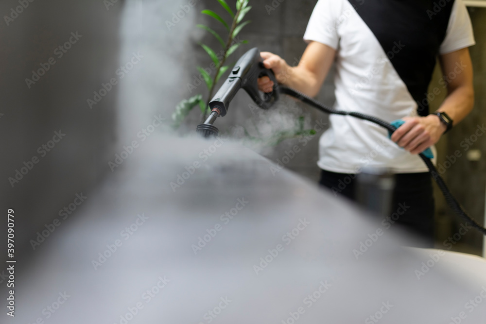 Worker of a cleaning company is cleaning the tiles in the bathroom with steam. Hot steam cleaning and desenfection