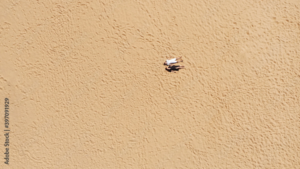 Aerial view of a young couple lying on the white sand. man and woman spend time together and travel through the desert Aerial view of a young couple lying on the white sand. man and woman spend time together and travel through the desert