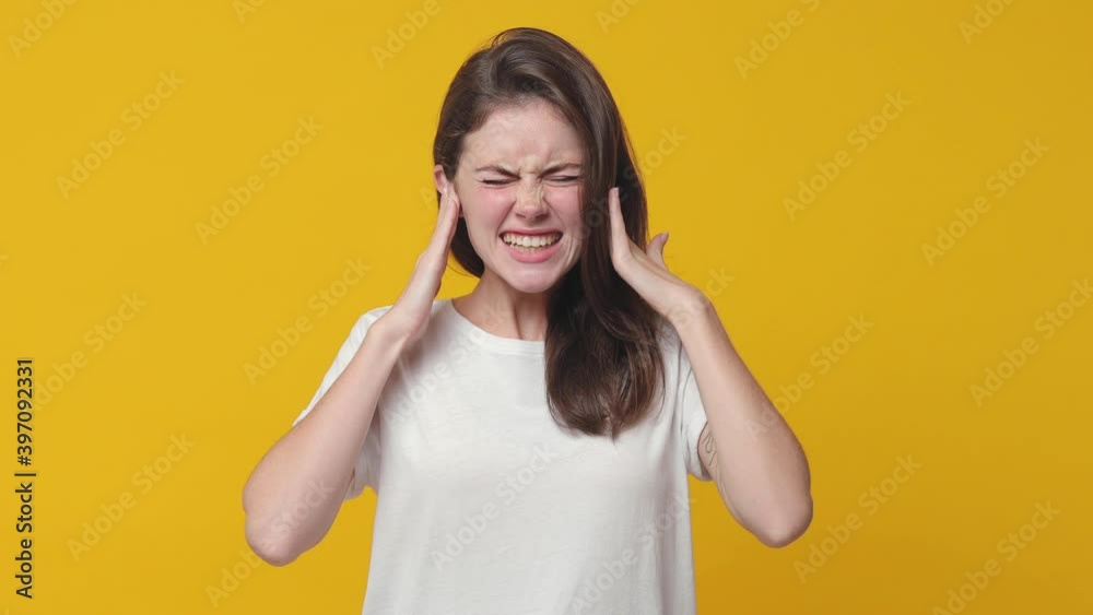 Shocked irritated brunette young woman 20s in basic white t-shirt posing isolated on yellow background studio. People lifestyle concept. Ask what covering ears with hands keeping eyes closed screaming Shocked irritated brunette young woman 20s in basic white t-shirt posing isolated on yellow background studio. People lifestyle concept. Ask what covering ears with hands keeping eyes closed screaming