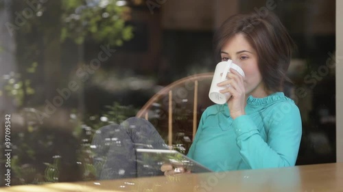 Woman drinking coffee and using digital tablet at window photo
