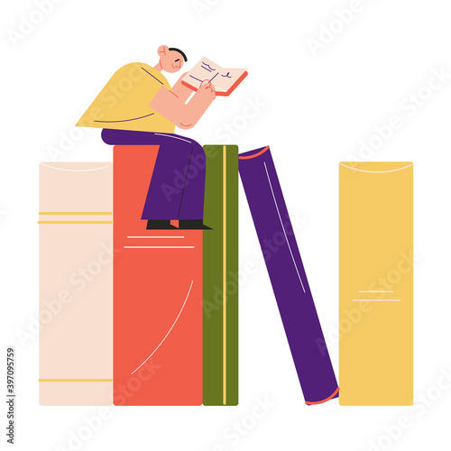 Happy young boy sitting on colorful books and reading story in book in library