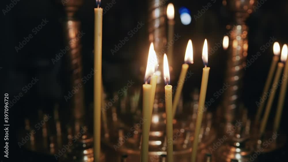 Thin yellow wax candles stand on a golden candlestick in a dark church and burn with a bright orange flame. Someone blew on them and two of them went out and only the smoke went up Thin yellow wax candles stand on a golden candlestick in a dark church and burn with a bright orange flame. Someone blew on them and two of them went out and only the smoke went up