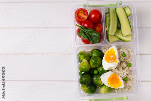 Vegetarian lunch. Tomatoes, cucumbers, Brussels sprouts, eggs and rice in food containers on a white wooden background with copy space; top view, flat lounger