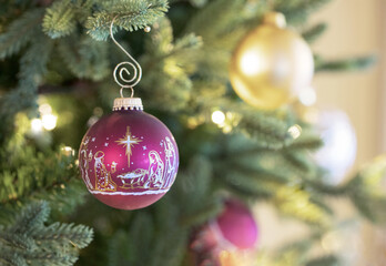 Original Christmas photograph of a golden Christian nativity scene on a burgundy and gold Christmas ball ornament hanging on the Christmas tree.
