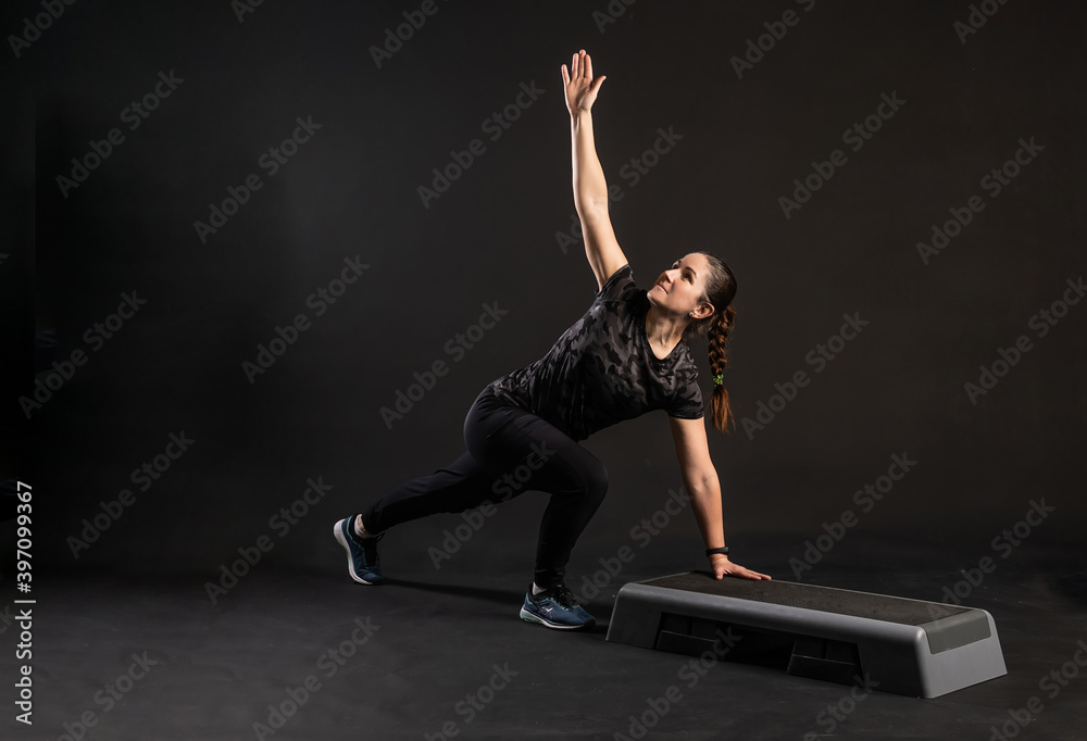 Fitness girl on the step on one hand platform, doing exercises. Engaged in sports on a black background Happy looking at the camera