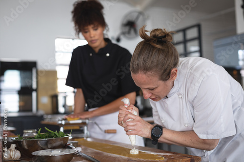Female senior caucasian chef adding fillings over ravioli pasta sheet at restaurant kitchen photo