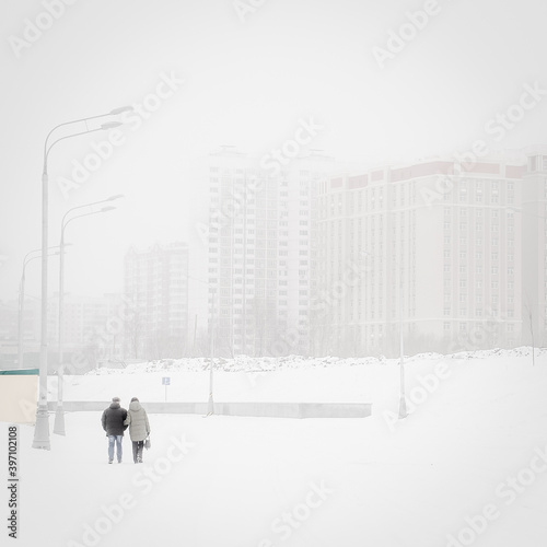 An adult couple walks through a snowy city. Loneliness in a big city.