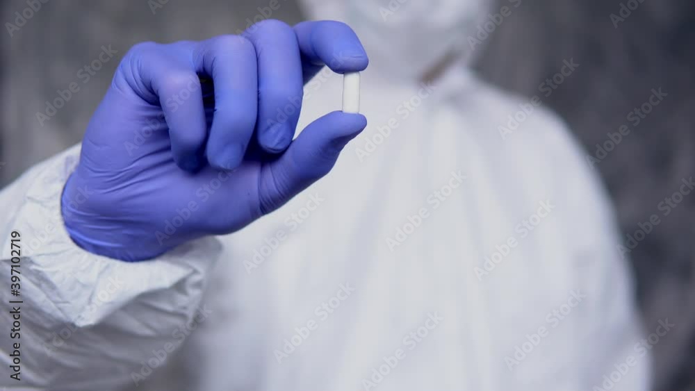 Doctor in white protective suit, medical mask and rubber gloves is holding a white pills as a medications from coronavirus pandemic threat. Epidemic, pandemic of coronavirus covid 19. Doctor in white protective suit, medical mask and rubber gloves is holding a white pills as a medications from coronavirus pandemic threat. Epidemic, pandemic of coronavirus covid 19.