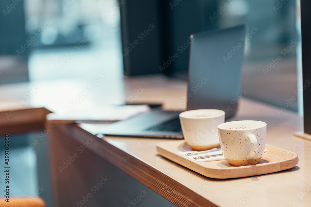 gray laptop, two cups of cappuccino coffee, Notepad, phone on a wooden table in a cafe in the city indoors in the daytime gray laptop, two cups of cappuccino coffee, Notepad, phone on a wooden table in a cafe in the city indoors in the daytime
