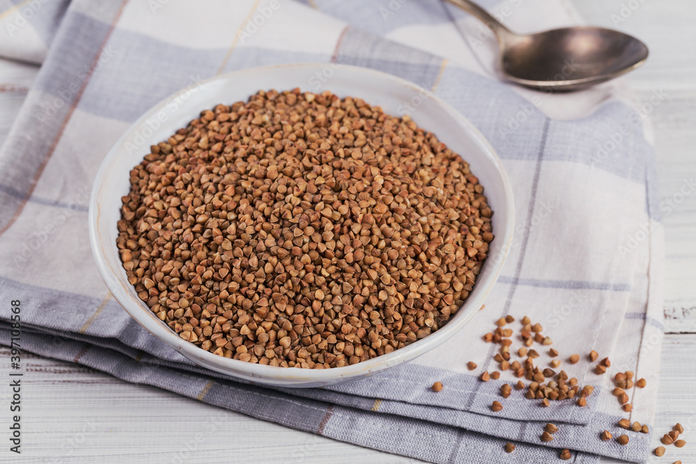 Bowl of dry raw buckwheat groats on a white wooden background. Cooking buckwheat porridge concept. Bowl of dry raw buckwheat groats on a white wooden background. Cooking buckwheat porridge concept.