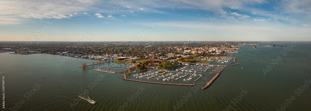 Incredible aerial city skyline wide angle panorama photograph of Sandusky, Ohio from the shoreline of the bay in Lake Erie with parks and harbors seen below on a sunny day as a boat passes by.