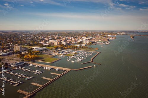 Incredible aerial city skyline panorama photograph of Sandusky, Ohio from the shoreline of the bay in Lake Erie with parks and harbors seen below on a sunny day.