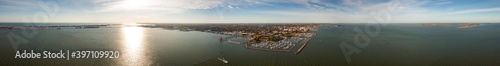 Incredible aerial city skyline wide angle panorama photograph of Sandusky, Ohio from the shoreline of the bay in Lake Erie with parks and harbors seen below on a sunny day as a boat passes by.