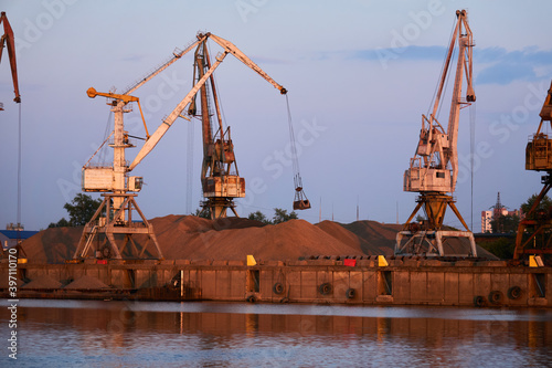 Schilderij op canvas level-luffing bulk-handling cranes load sand onto a barge in a river port in the