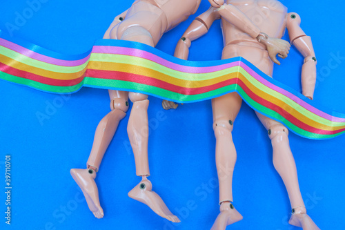A gay couple of male dolls lying on the bed with the rainbow flag LGTB pride