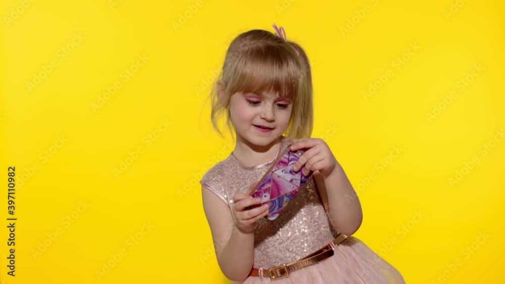 Little girl using smartphone. Portrait of child texting on smartphone. Kid enthusiastically playing games on mobile phone isolated on yellow background in studio. Technology for children. Slow motion Little girl using smartphone. Portrait of child texting on smartphone. Kid enthusiastically playing games on mobile phone isolated on yellow background in studio. Technology for children. Slow motion