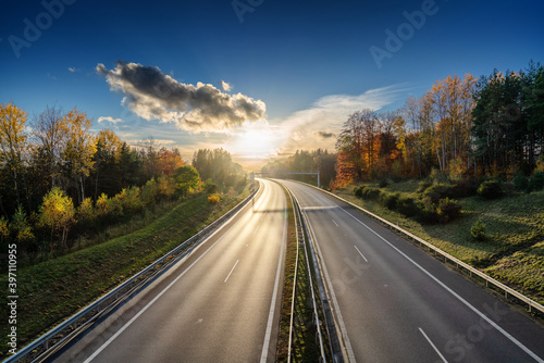 Empty asphalt highway bending into a bend in an autumn forested landscape at sunset