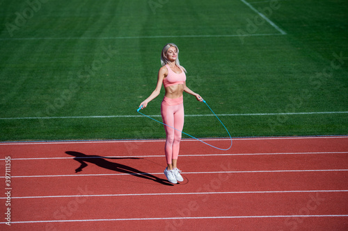 woman with sexy fitness body in sportswear training on stadium with skipping rope, full of energy