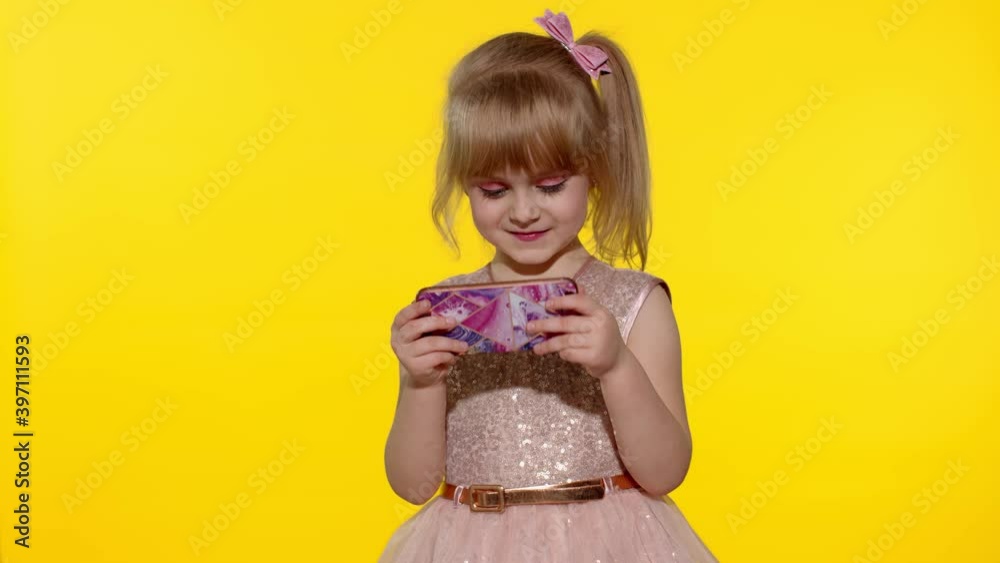 Little girl using smartphone. Portrait of child texting on smartphone. Kid enthusiastically playing games on mobile phone isolated on yellow background in studio. Technology for children. Slow motion Little girl using smartphone. Portrait of child texting on smartphone. Kid enthusiastically playing games on mobile phone isolated on yellow background in studio. Technology for children. Slow motion