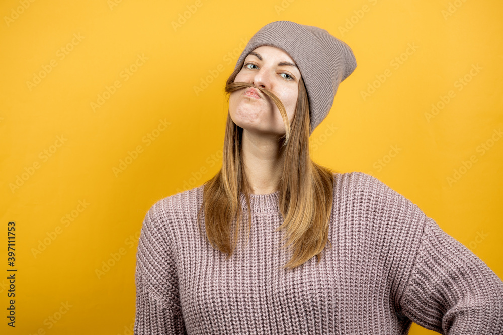 funny caucasian young woman with mustache made by her hair over yellow background. isolated yellow background. person warm dressed funny caucasian young woman with mustache made by her hair over yellow background. isolated yellow background. person warm dressed