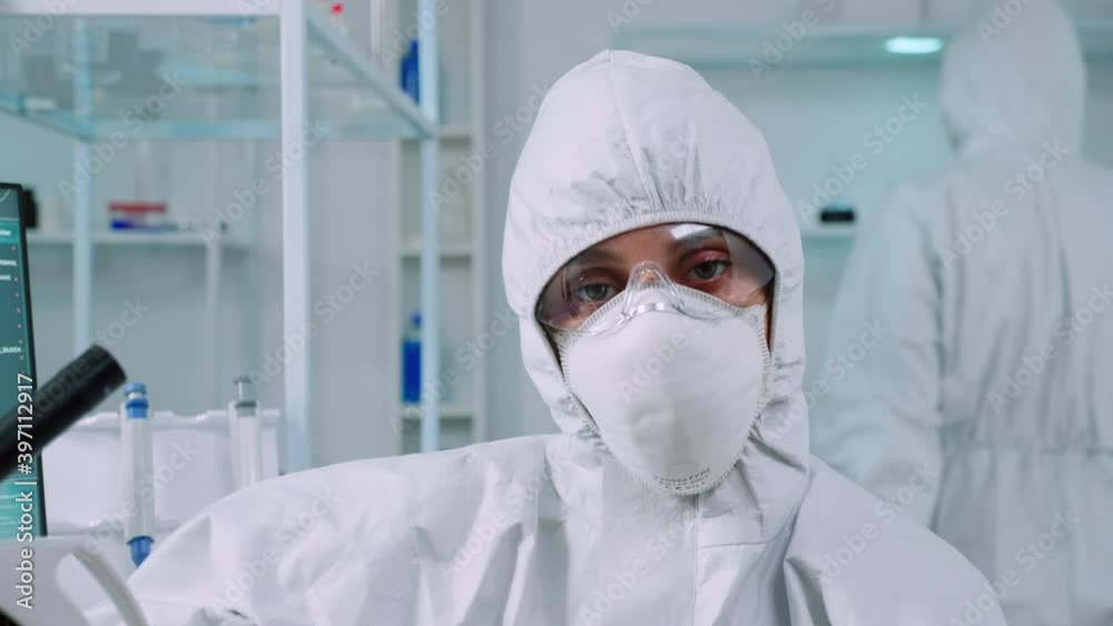 Portrait of tired scientist in coverall looking at camera sitting in modern equipped laboratory. Team of doctors examining virus evolution using high tech and chemistry tools for vaccine development. Portrait of tired scientist in coverall looking at camera sitting in modern equipped laboratory. Team of doctors examining virus evolution using high tech and chemistry tools for vaccine development.