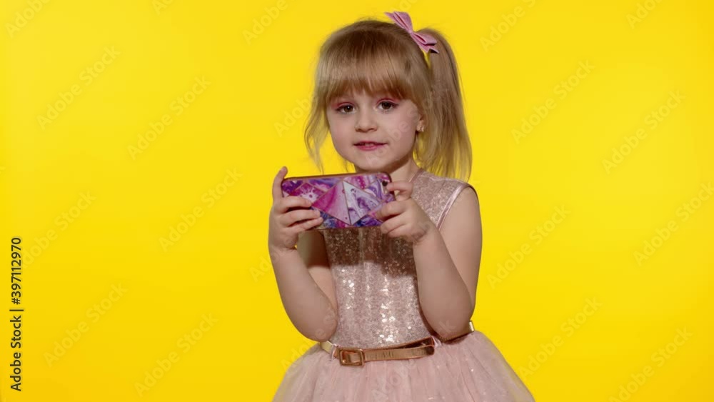 Little girl using smartphone. Portrait of child texting on smartphone. Kid enthusiastically playing games on mobile phone isolated on yellow background in studio. Technology for children. Slow motion Little girl using smartphone. Portrait of child texting on smartphone. Kid enthusiastically playing games on mobile phone isolated on yellow background in studio. Technology for children. Slow motion