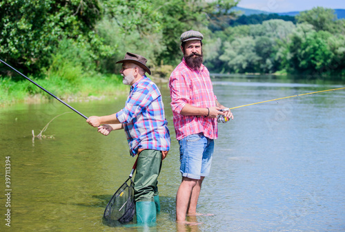 partnership. father and son fishing. two happy fisherman with fishing rod and net. male friendship. family bonding. summer weekend. mature men fisher. hobby and sport activity. Trout bait