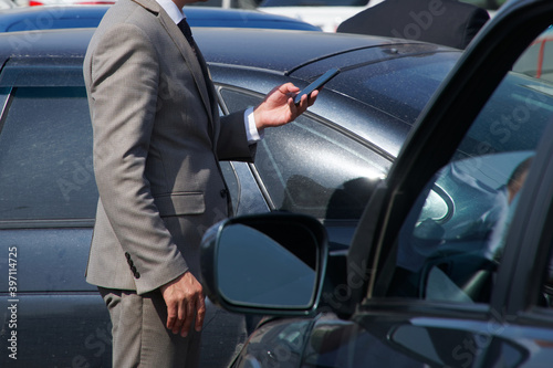 A man in a business suit - an official or a businessman talking on a smartphone among black cars. Business meeting or conversation. Solving problems and tasks © slexp880