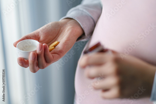 Close up on midsection of unknown pregnant caucasian woman hold bottle in hands taking medicine drugs or vitamin supplements at home - pregnancy and supplementation concept copy space
