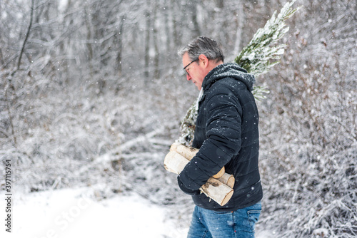 Man carrying logs and pine branches in the snow