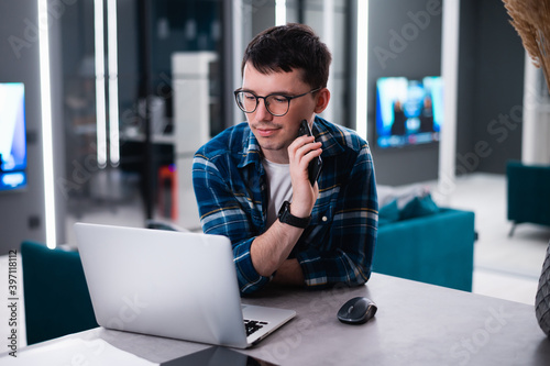 View of concentrated talented skilled male focused on screen of laptop computer, reads necessary information for creating budget report